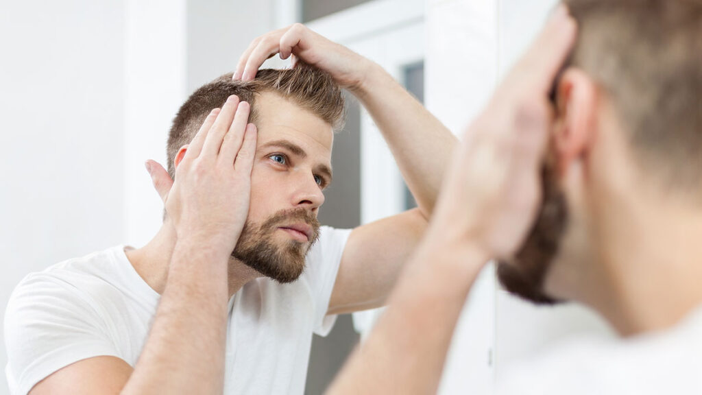Hombre joven preocupado por su cabello frente al espejo